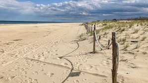 En sandstrand med fotspår, ett trästaket och hus i bakgrunden.