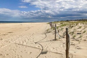 Ein Sandstrand mit Fußspuren, ein Holenzaun und Häuser im Hintergrund.