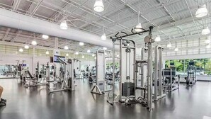 Ett rymligt gym med olika träningsmaskiner, stora fönster och ett högt tak.