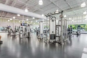Ein großzügiges Fitnessstudio mit verschiedenen Trainingsgeräten, großen Fenstern und hoher Decke.