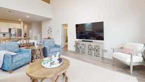 Een ruime woonkamer met een flatscreen-tv, twee banken, een eethoek en een keuken op de achtergrond.