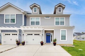 A two-story residential building with a garage, a covered driveway, and a blue front door. - Friendship Creek dog-friendly townhome with pool, dog parks, bikes, & W/D (Frankford)