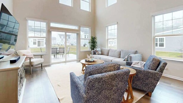 Een ruime woonkamer met een groot raam, een bank, twee fauteuils, een salontafel en een televisie.
