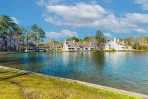 A lakeside view with a row of white buildings, a wooden dock, and a clear sky. - Sea Colony condo with access to pools, tennis courts, gym, & a private beach (Bethany Beach)