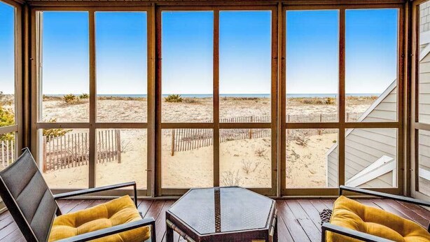 Una stanza con ampie finestre, un soffitto in legno e vista su una spiaggia sabbiosa.