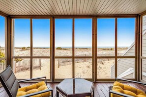 Une pièce dotée de grandes fenêtres, d’un plafond en bois et offrant une vue sur une plage de sable.