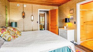 Una camera da letto con soffitto in legno, un letto con cuscini a motivi, un comodino con lampada e un armadio.