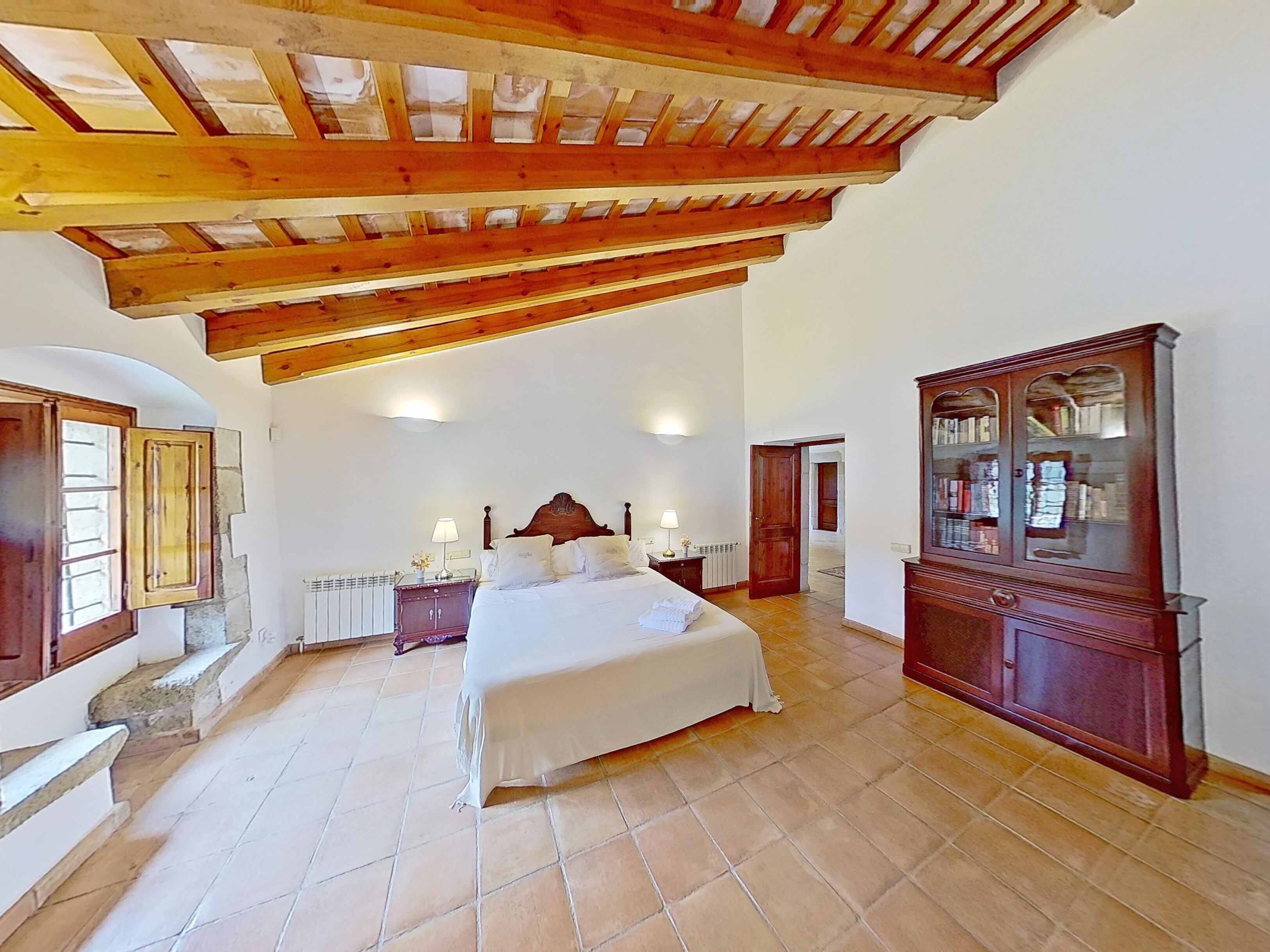 Een slaapkamer met een groot bed, houten balken in het plafond, een radiator, een houten kast en een stenen trap.