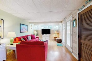 A living room with a red sofa, a television, and a small table with a lamp. - Town of Dewey Beach dog friendly condo with washer/dryer & free WIFI (Dewey Beach)