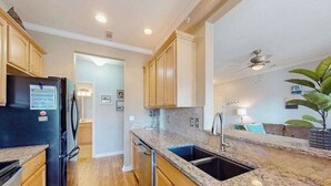 A kitchen with wooden cabinets, a black refrigerator, granite countertops, and a ceiling fan. - Beautiful condo near ocean with pool, fast WiFi, central AC & washer/dryer (Lewes)