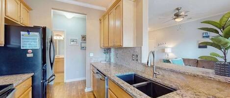 A kitchen with wooden cabinets, a black refrigerator, granite countertops, and a ceiling fan.