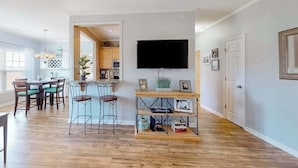A modern living room with a dining area, a kitchen in the background, and a mounted TV. - Beautiful condo near ocean with pool, fast WiFi, central AC & washer/dryer (Lewes)