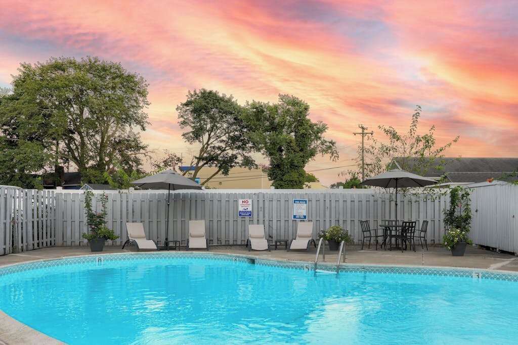 A swimming pool with lounge chairs and a table, surrounded by a wooden fence.