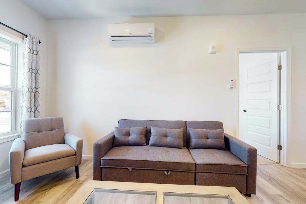 Uma sala de estar com sofá, uma poltrona e aparelho de ar condicionado.