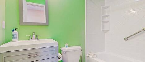 Un baño con pared verde, sanitarios blancos, un inodoro y una bañera.