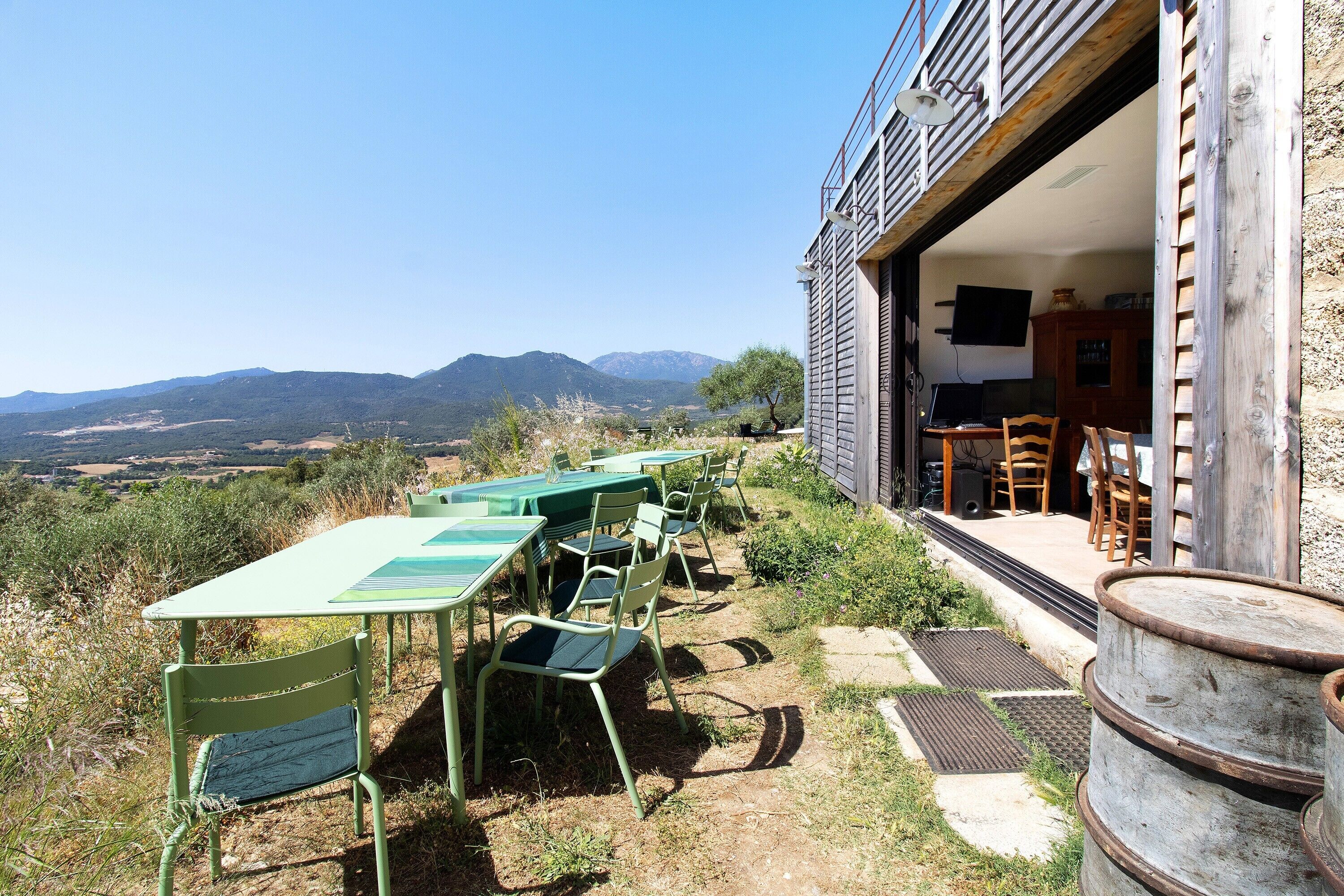 An outdoor dining area with a table and chairs, a wooden barrel, and a view of mountains.