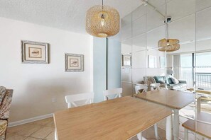 A modern interior with a wooden dining table, white chairs, and a hanging woven light fixture. - Sea Colony 7th floor condo with gym, shared sauna, and ocean views (Bethany Beach)