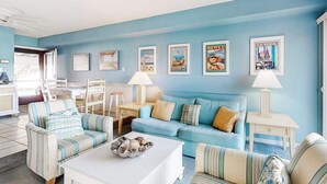 Een woonkamer met een blauwe wand, gestreepte banken, een salontafel met decoratieve objecten en ingelijste foto's.