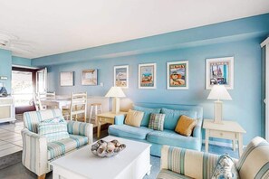 Ein Wohnzimmer mit blauer Wand, gestreifter Couchgarnitur, einem Couchtisch mit Dekoration und gerahmten Bildern.