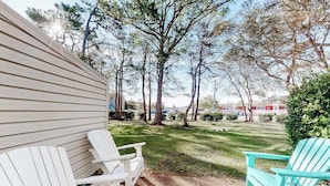 Een terras met Adirondack stoelen, een gazon en bomen.