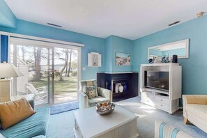 Ein Wohnzimmer mit einer Couch, Couchtisch, Fernseher, Kamin und Blick durch eine Schiebetür.