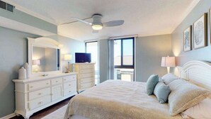 A bedroom with a bed, dresser, vanity, ceiling fan, and large windows. - Sea Colony oceanfront 3rd floor condo w/ shared sauna, basketball court, balcony (Bethany Beach)