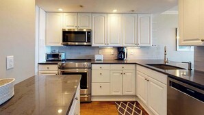 A modern kitchen with white cabinets, stainless steel appliances, and a granite countertop. - Sea Colony oceanfront 3rd floor condo w/ shared sauna, basketball court, balcony (Bethany Beach)