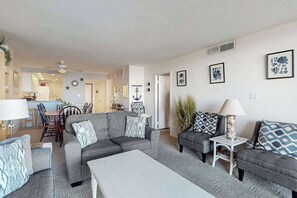 A living room with grey sofas, a white coffee table, and a dining area in the background. - Sea Colony 5th floor condo w/ balcony and gym - partial ocean view (Bethany Beach)