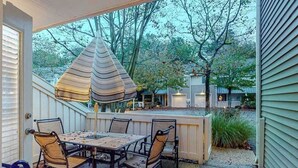 An outdoor patio with a table and chairs, a hanging light fixture, and a view of trees and a house in the background. - Sea Colony Tennis townhouse w/ gym, tennis court, free WiFi, and balcony (Bethany Beach)