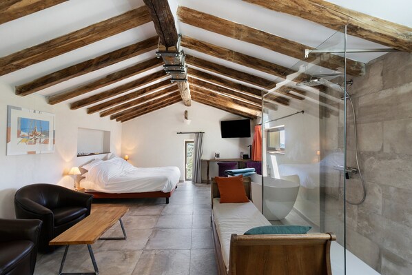 A modern bedroom with a sloped ceiling, a bed, a sofa, a desk, and a glass shower enclosure.