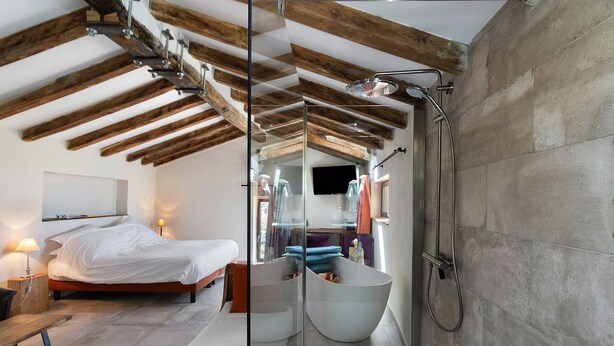 Un dormitorio moderno con una cama grande, un separador de vidrio, una bañera y una ducha.