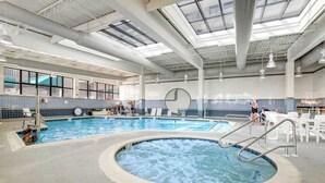 Una piscina interior con un jacuzzi, sillones de descanso y un amplio ventanal.