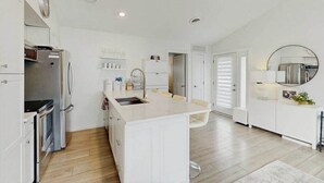 Una cocina moderna con armarios blancos, una isla central, electrodomésticos de acero inoxidable y un espejo redondo sobre el fregadero.