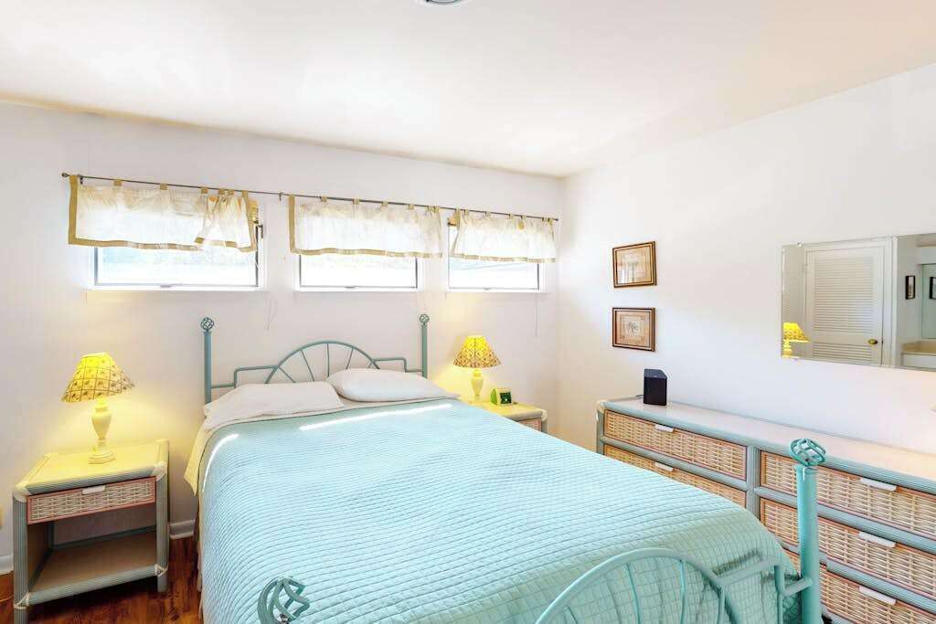 A bedroom with a bed, two bedside tables, a nightstand, a lamp, a mirror, and a window with curtains.