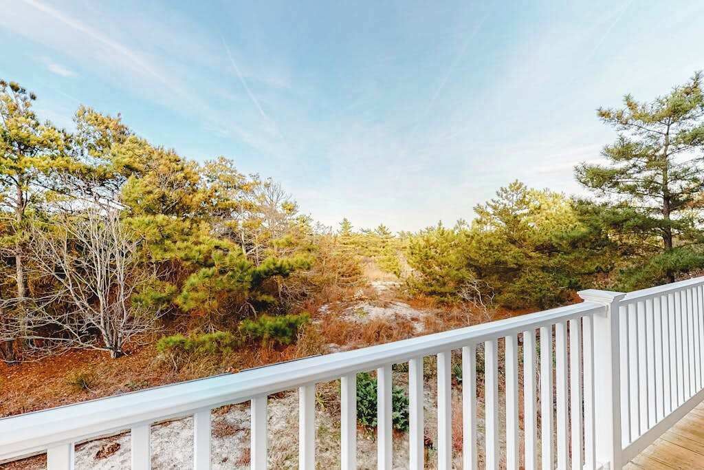 Une terrasse en bois dotée d’une rambarde, qui offre une vue sur un paysage naturel composé d’arbres et d’arbustes.