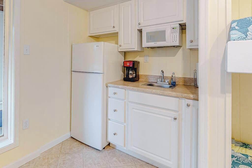 A compact kitchen with white cabinets, a built-in microwave, a coffee maker, and a sink.