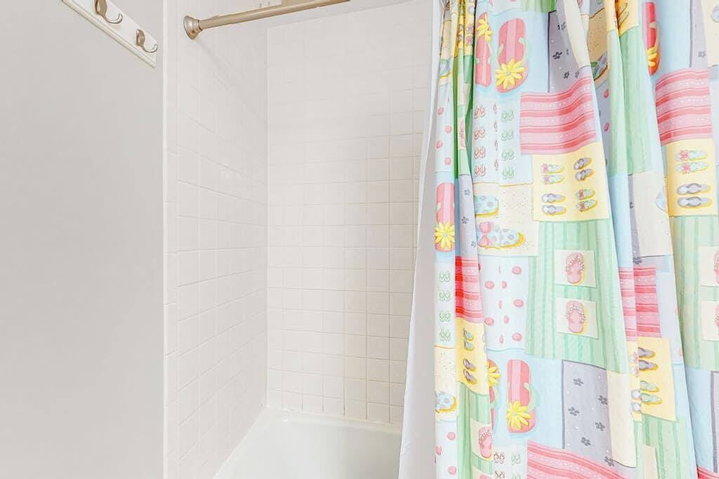 Une salle de bain avec des murs carrelés de carreaux blancs, un rideau de douche à motifs colorés et un porte-serviettes en métal.