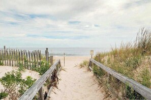 Ein Sandweg am Strand mit Holzwailfarschen und einem Wegweiser.