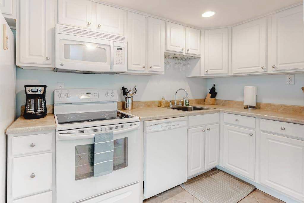 A kitchen with white cabinets, a microwave, a stove, a dishwasher, and a coffee maker.