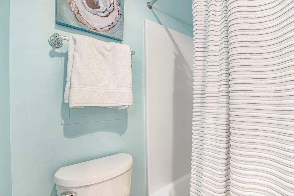 Ein Badezimmer mit Toilette, Handtuchhalter mit Handtuch, einer Glasarbeit und einem gestreiften Duschvorhang.