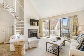 Ein Wohnzimmer mit Kamin, einem weißen Sofa, einem Couchtisch, einem Korbsessel und einer Wendeltreppe.