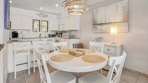 Una cucina moderna con mobili bianchi, un tavolo rotondo con sottopiatti intrecciati e una lampada a sospensione.
