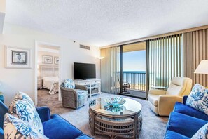 Habitación de hotel con balcón, televisión de pantalla plana, mobiliario de mimbre y vista a la playa.