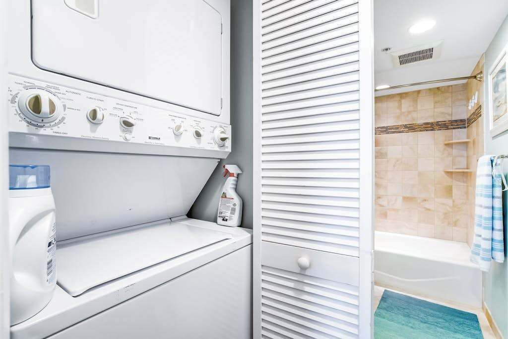 Ein Waschbereich mit Waschmaschine und Trockner, einer Waschmittelflasche sowie ein Badezimmer mit Badewanne und Dusche.