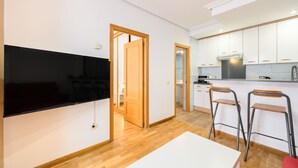 A modern kitchen with white cabinets, a built-in oven, and a dining area with a TV and bar stools. - (VAL203E) 1 bedroom apartment in the center of Madrid (Madrid)