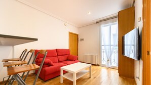 A room with a red sofa, a white table, and a TV on the wall. - (VAL203E) 1 bedroom apartment in the center of Madrid (Madrid)