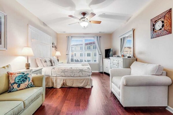 A bedroom with a bed, a chair, a desk, a ceiling fan, and a window with curtains.
