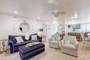 A living room with a sofa, armchair, ottoman, and a ceiling fan. - Sea Colony Condo w/ Private Beach, WiFi, Shared Pool/Hot Tub, Central AC, & Deck (Bethany Beach)