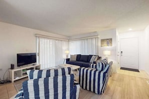 A living room with a sofa, armchairs, a TV, and a lamp. - Sea Colony Condo Near Beach w/Shared Hot Tubs/Pools/Gym/Sauna/WiFi/AC/Deck + W/D (Bethany Beach)