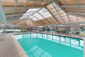 An indoor swimming pool with a glass ceiling, surrounded by lounge chairs and a view of the outside. - Salt Pond house with W/D, pools, & hot tub - near beach & dining (Bethany Beach)